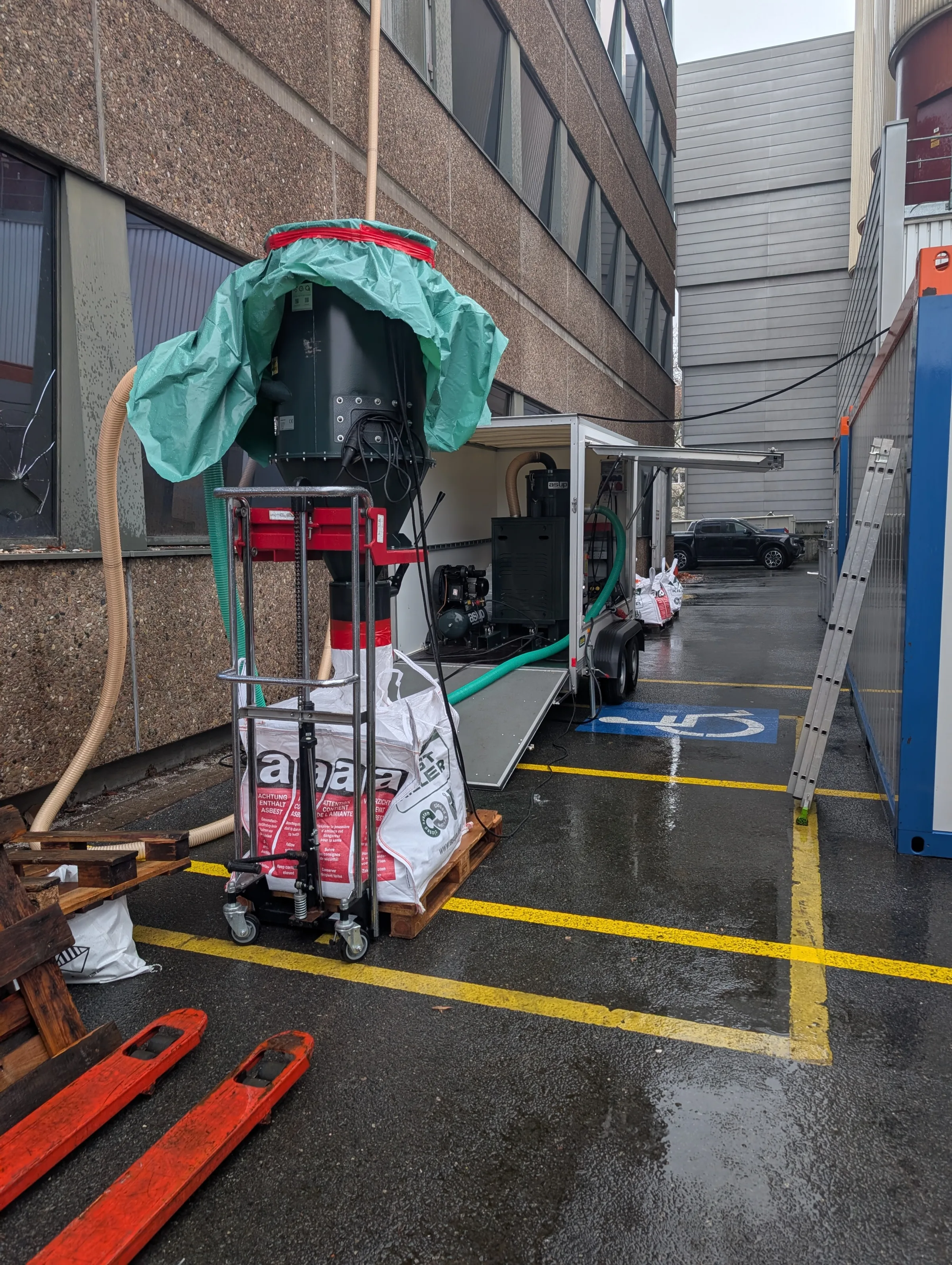 Unterdruckanlage mit gruener Plane und Container vor einem Buerogebaeude, Schwarz-Weiss-Bereich fuer Asbestsanierung